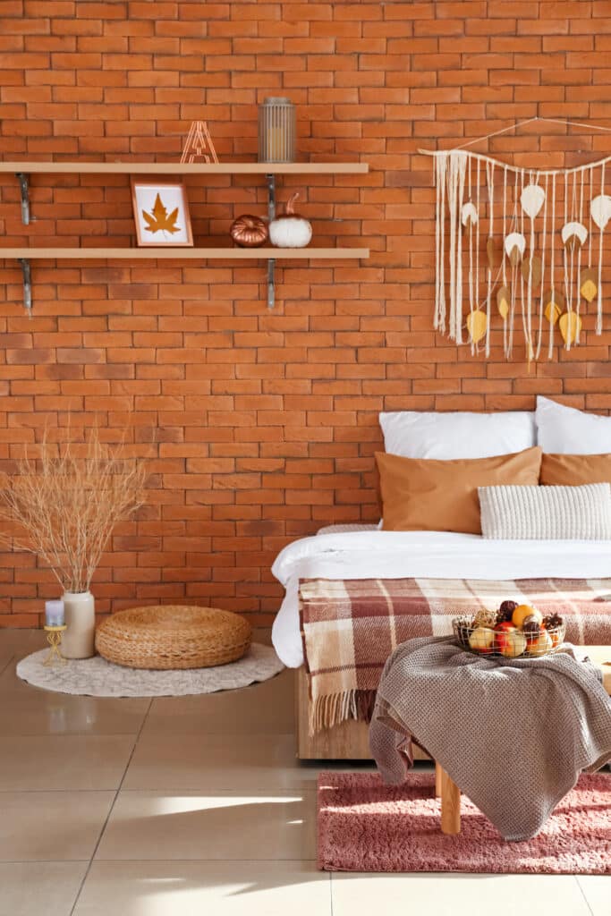 Décoration Chambre Automnale Briques et Macramé Doux Chambre décorée d'automne avec mur en briques, étagère avec citrouilles, macramé feuille, et literie couleur terre cuite.