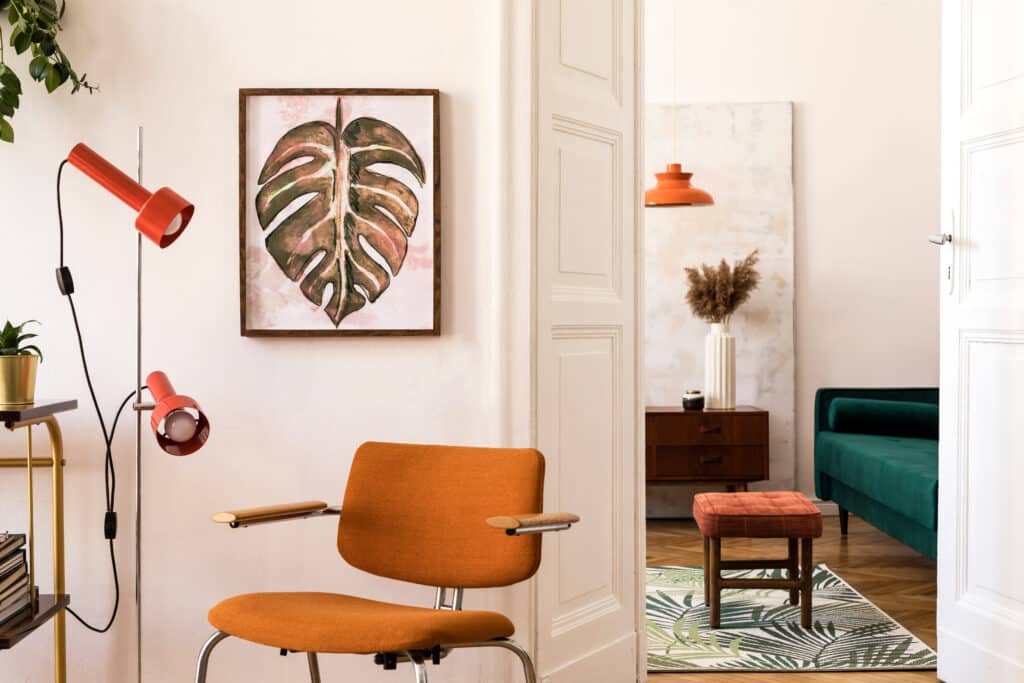 Décoration Mid-Century : Orange, Vert et Monstera Intérieur moderne avec chaise orange et lampe rouge, vue sur un salon vert émeraude à travers une porte blanche.