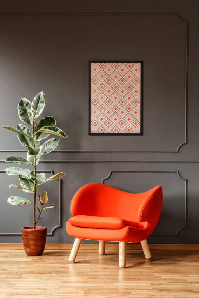 Décoration Salon : Fauteuil Orange et Mur Gris Fauteuil orange vif moderne près d'un ficus panaché devant un mur gris foncé avec moulures et un tableau géométrique.