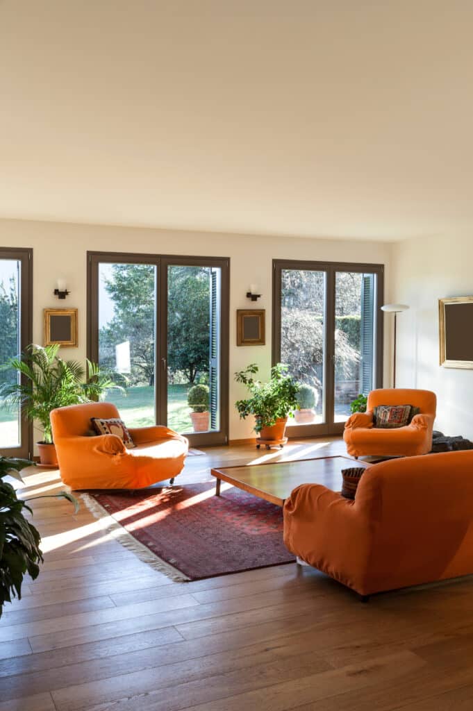 Salon lumineux avec fauteuils orange et vue jardin Salon lumineux avec mobilier orange, grandes baies vitrées donnant sur un jardin verdoyant et parquet en bois.