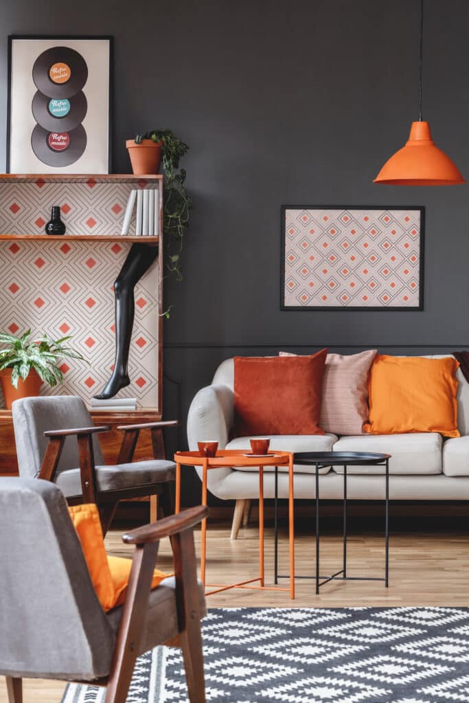 Décor Rétro-Moderne : Salon Chic avec Touches Orange Salon moderne avec mur gris foncé, fauteuils vintage gris, canapé clair, tables d'appoint orange et noires. Affiche "Retro music".