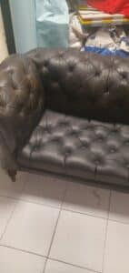 Canapé Chesterfield en cuir marron foncé capitonné, style vintage avec accoudoirs arrondis sur sol carrelé.