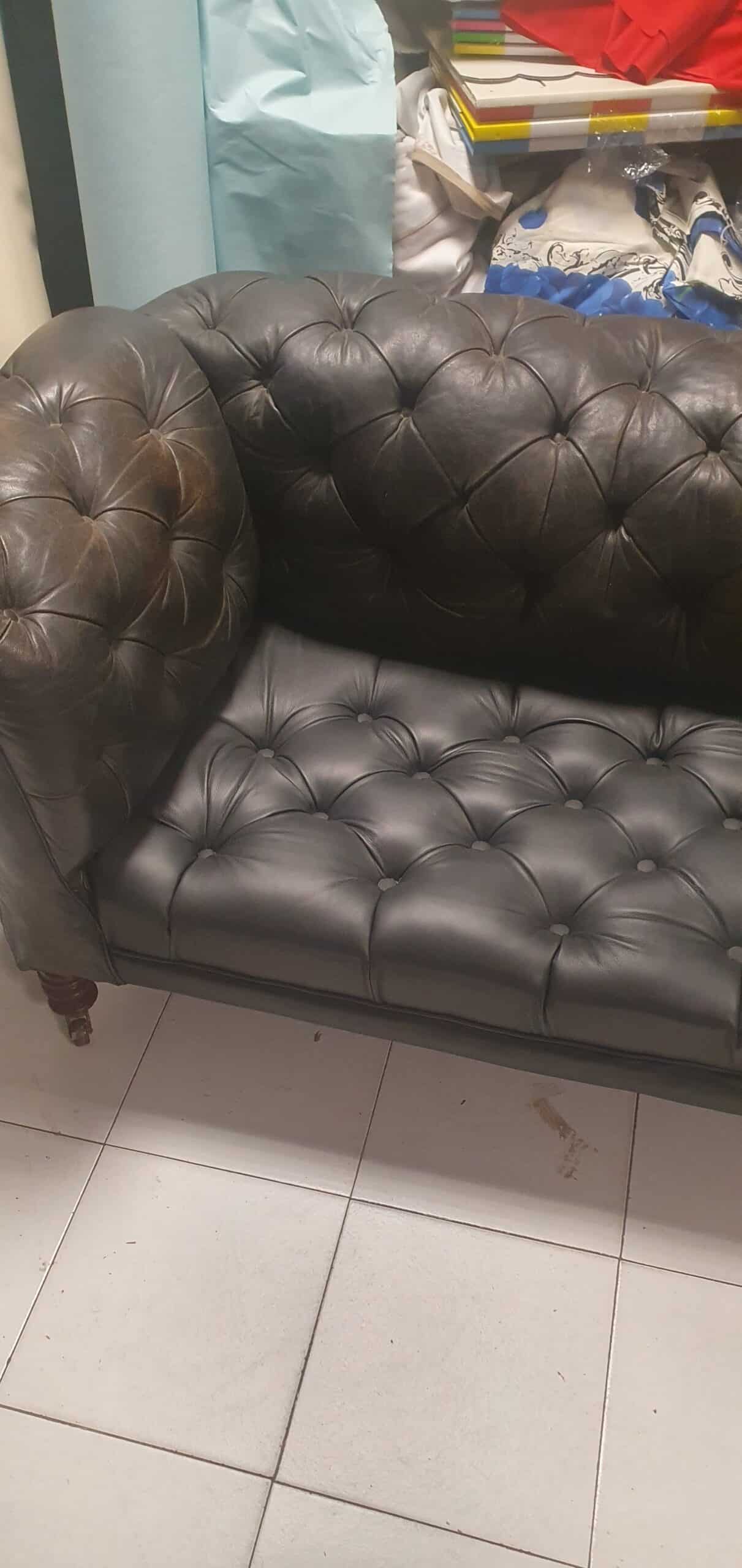 Canapé Chesterfield en cuir marron foncé capitonné, style vintage avec accoudoirs arrondis sur sol carrelé.