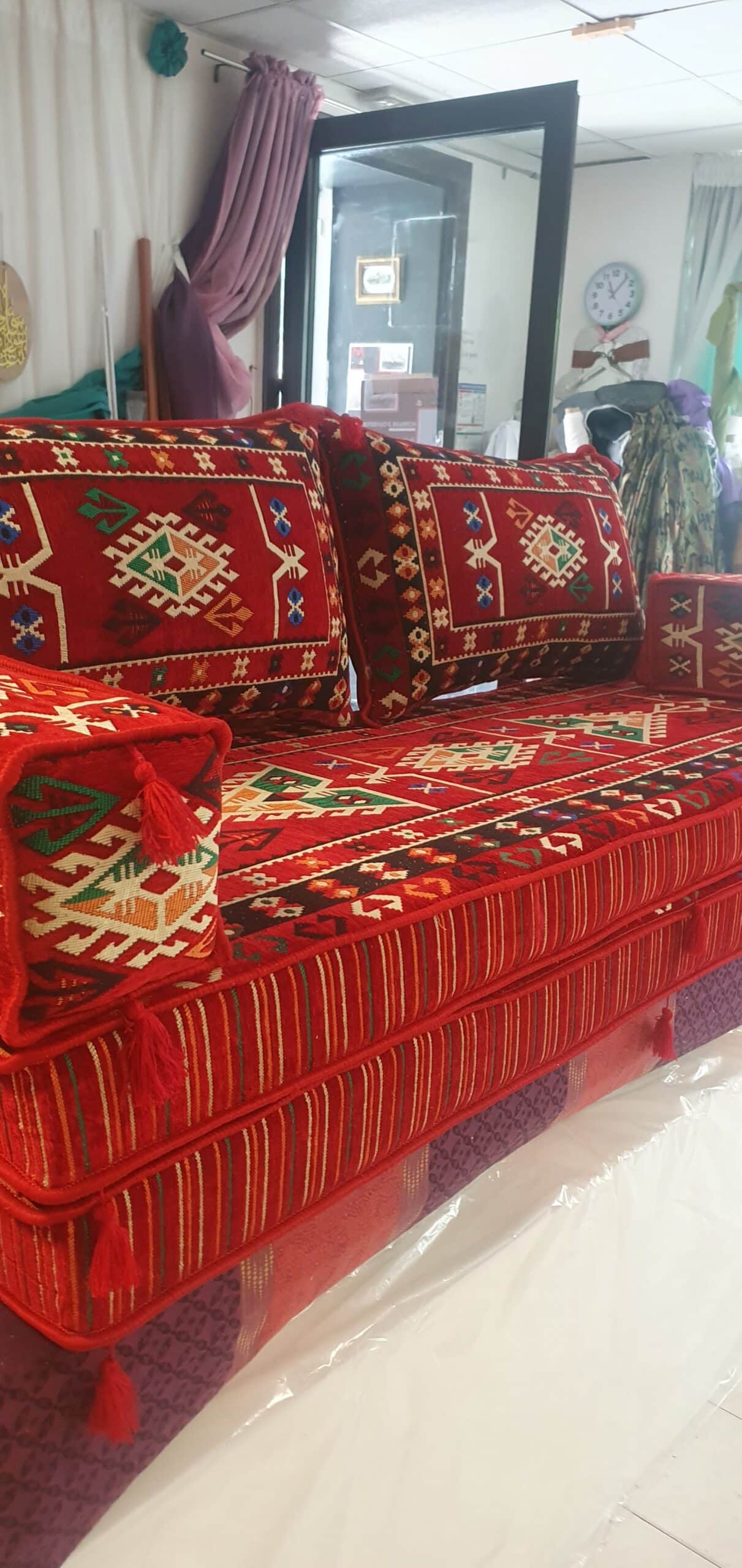 Canapé majlis oriental rouge aux motifs géométriques avec coussins et pompons pour un salon traditionnel.