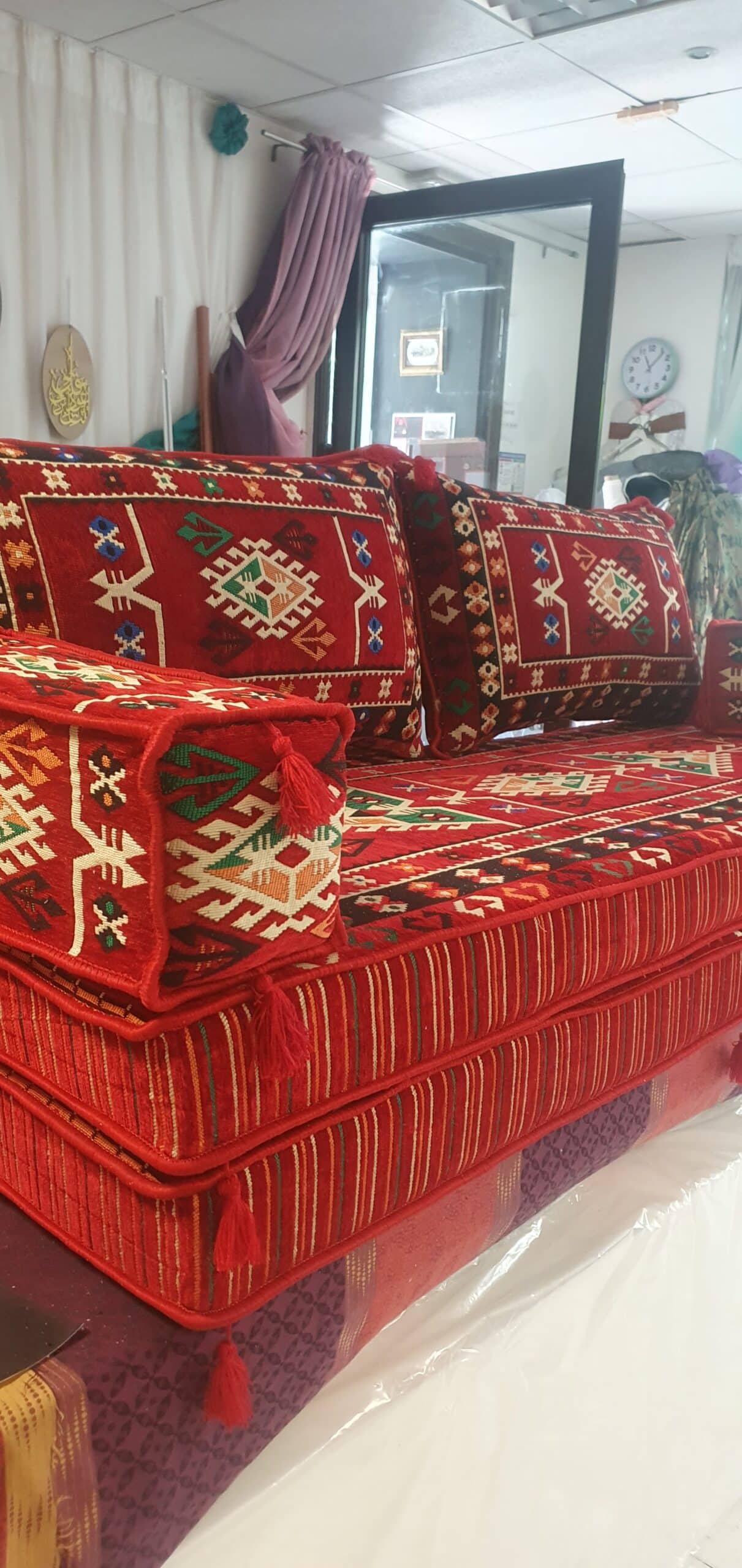 Salon oriental majlis rouge avec motifs kilim traditionnels et coussins à pompons pour assise au sol.
