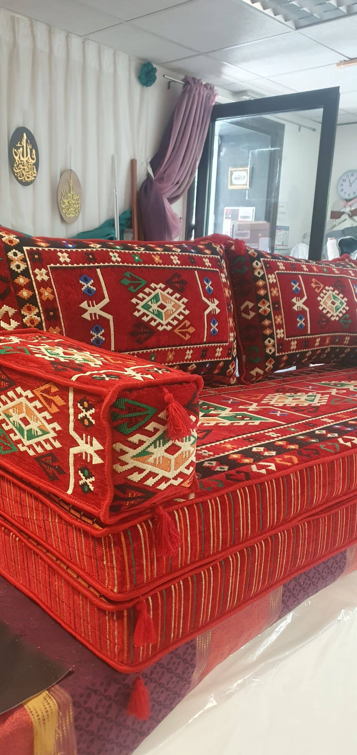 Majlis traditionnel rouge aux motifs géométriques colorés avec coussins rectangulaires et pompons décoratifs.